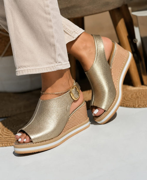 Primer plano de modelo luciendo unas sandalias de plataforma tipo espadrille en color oro metalizado, con correa ajustable al tobillo y suela de yute.