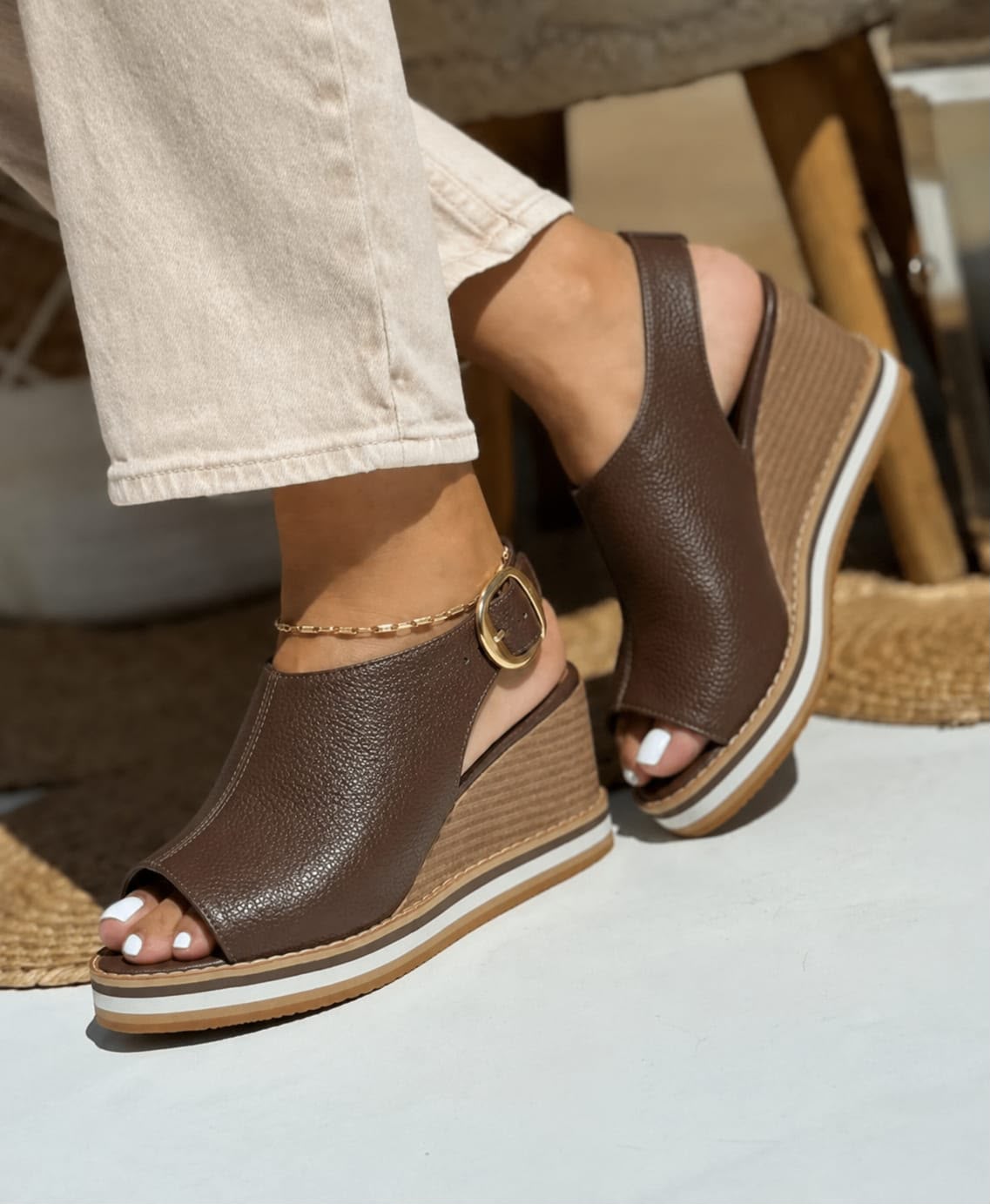 Primer plano de modelo luciendo sandalias de plataforma tipo cuña en color marrón con diseño cerrado en el talón, correa ajustable con hebilla dorada y suela cómoda de doble tono.