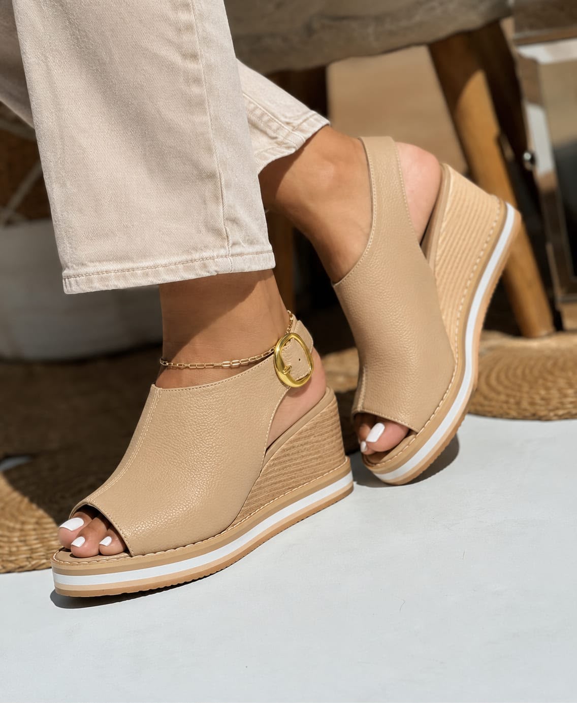 Primer plano de modelo luciendo sandalias de plataforma tipo cuña en color taupe con diseño cerrado en el talón, correa ajustable con hebilla dorada y suela cómoda de doble tono.