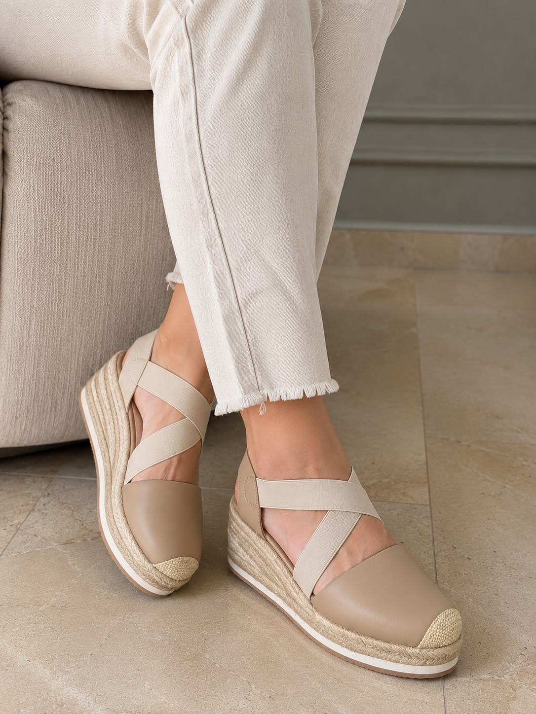 Modelo luciendo unas sandalias tipo espadrille en color taupe con plataforma de yute y correas elásticas cruzadas, combinadas con un pantalón blanco.